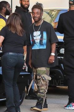 a man standing next to a woman in front of a car with other people around him