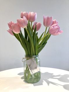 pink tulips in a mason jar with a price tag on the label, sitting on a white table