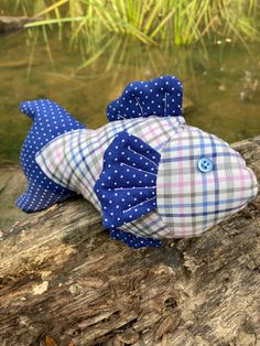 two stuffed fish sitting on top of a log next to a body of water with grass in the background