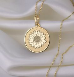 a necklace with a sunflower on it sitting on top of a white cloth next to a gold chain