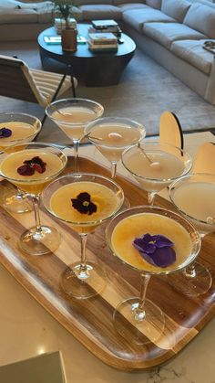 several glasses filled with different types of drinks on a wooden serving tray in front of a couch