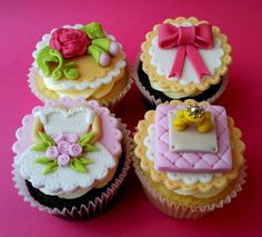 four decorated cupcakes sitting on top of a pink table