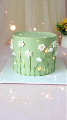 a green cake decorated with daisies on a white tablecloth and lights in the background