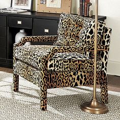 a leopard print chair sitting in front of a desk with a lamp and pictures on the wall