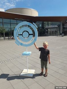 a young boy standing next to a blue clock on top of a metal pole in front of a building