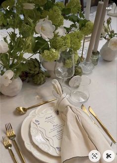 the table is set with white and gold place settings, silverware, and flowers