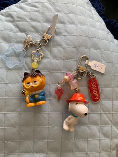 two key chains that are laying on top of a bed with charms attached to them