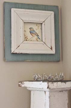 a blue and white bird sitting on top of a mantle next to a framed painting