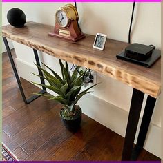 a wooden table topped with a plant next to a clock and phone on top of it