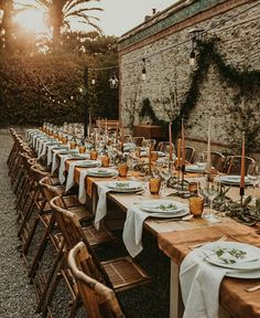 a long table is set up with place settings for an outdoor dinner party in the evening