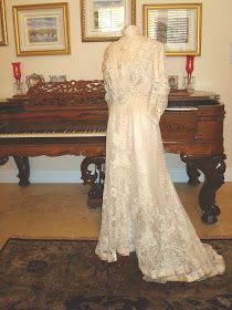 an antique dress is on display in front of a piano and framed pictures with candles