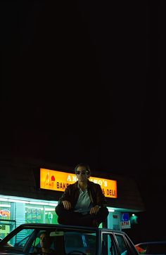 a man sitting on top of a car in front of a gas station at night