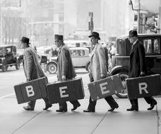 three men walking down the street carrying suitcases that say beer and two men in top hats