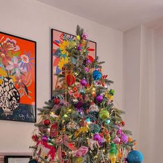 a brightly colored christmas tree with ornaments on it in front of two framed art pieces