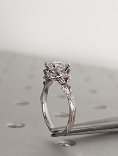 a close up of a diamond ring on top of a silver surface with drops of water