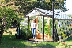 a woman standing in a small greenhouse with plants growing inside and doors open to the outside