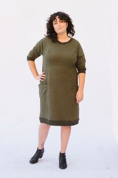 a woman standing in front of a white background wearing a green dress and black boots