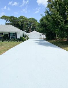 a driveway leading to a white house with trees in the background