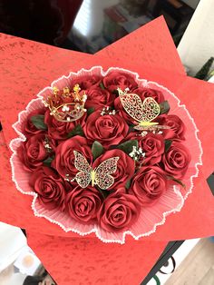 a bouquet of red roses in a paper box with butterflies on it, sitting on top of a table