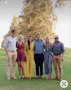 a group of people standing next to each other on a lush green field with trees in the background