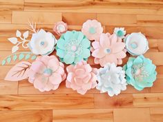 paper flowers are laid out on a wooden floor, with leaves and flowers in pastel colors