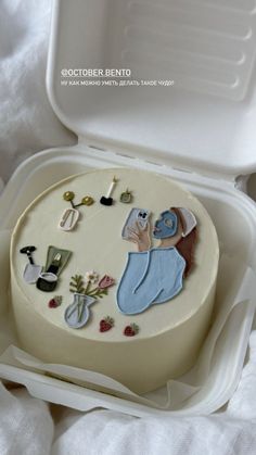 a decorated cake in a white box on top of a bed with the lid open