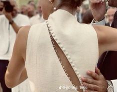 the back of a woman's dress with pearls on it and people in the background