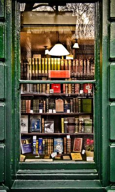 an open window with books on the shelves and lamps above it in front of a green building