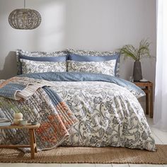 a bed with blue and white comforters in a room next to a table on the floor