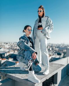 two women standing on top of a building with their arms around each other and looking off into the distance