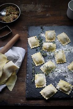 homemade ravioli with herbs and parmesan cheese on a slate board next to baking utensils