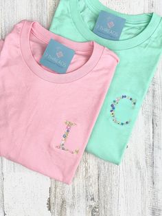 These sweet floral monograms are the cutest! Choose up to 4 flower colors to be featured in your personalized stitching. Color placement will vary and each monogram is unique. Leaves are green unless otherwise specified. T-Shirts are unisex sizing Bella Canvas. Tie it up, crop it, tuck it or wear with leggings for an oversized comfy look. Girls Monogram Shirts, Vinyl Monogram Shirt, Spring T-shirt With Multicolor Embroidered Text, Blue Tops With Letter Embroidery For Spring, Multicolor Embroidered Text T-shirt For Spring, Spring Tops With Letter Embroidery And Relaxed Fit, Pink Tops With Embroidered Text For Summer, Pink Summer Top With Embroidered Text, Pink Top With Embroidered Text For Summer