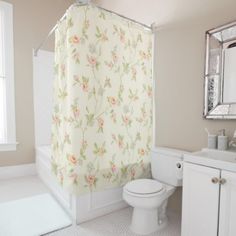 a white toilet sitting next to a sink in a bathroom under a shower curtain with pink flowers on it