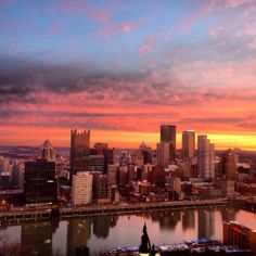 the city skyline is lit up at sunset with pink clouds in the sky and water below