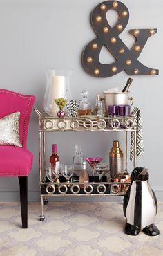 a pink chair sitting next to a table with bottles and glasses on it