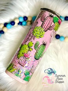 a pink tumbler with cactus designs on it sitting next to some beads and pearls