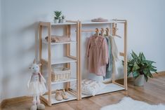 a wooden shelf with clothes and shoes on it next to a potted plant in a white room