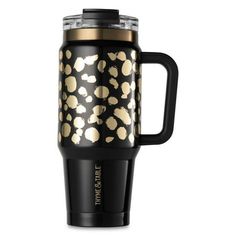 a black and gold travel mug with polka dots on the lid, in front of a white background