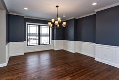 an empty room with hard wood flooring and dark blue walls, white trim around the windows