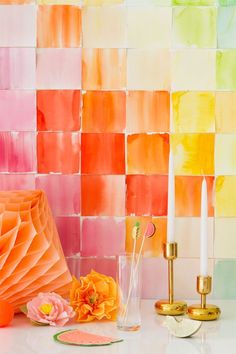 some candles are sitting on a table next to colorful wall tiles and vases with flowers in them