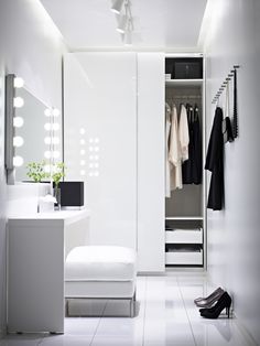 a white closet with clothes hanging on the wall and a bench in front of it