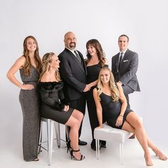 a group of people posing for a photo in formal wear with one woman sitting on a stool