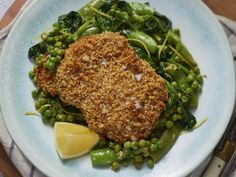 a white plate topped with green beans and meat next to a lemon wedge on top of a wooden table