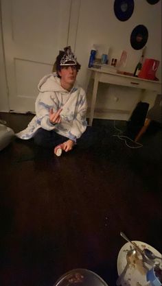 a young man sitting on the floor in front of a table with plates and bowls