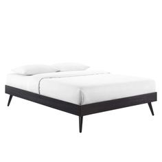 the bed is made up with white sheets and black wood legs on top of it