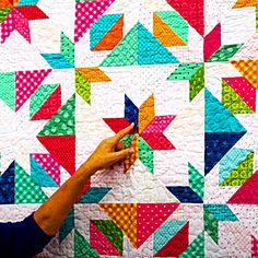 a woman is making a colorful quilt on the wall with one hand and pointing at it