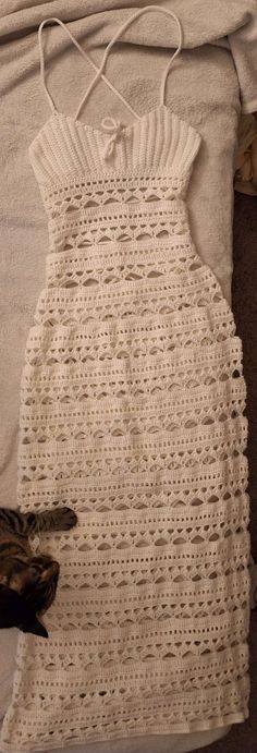 a cat laying on top of a bed next to a white crocheted dress