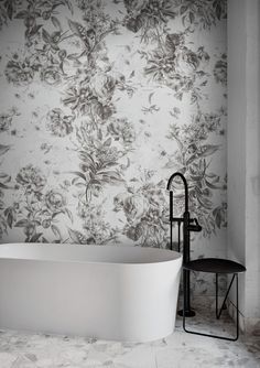 a white bathtub sitting next to a wall with flowers on it and a black faucet