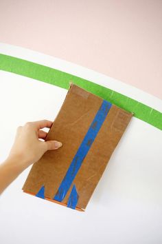 a person holding a piece of brown paper with blue lines on it and green tape around the edge