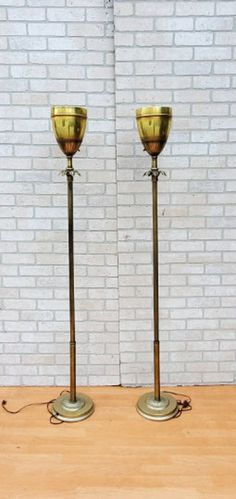 two brass candlesticks on wooden table next to brick wall